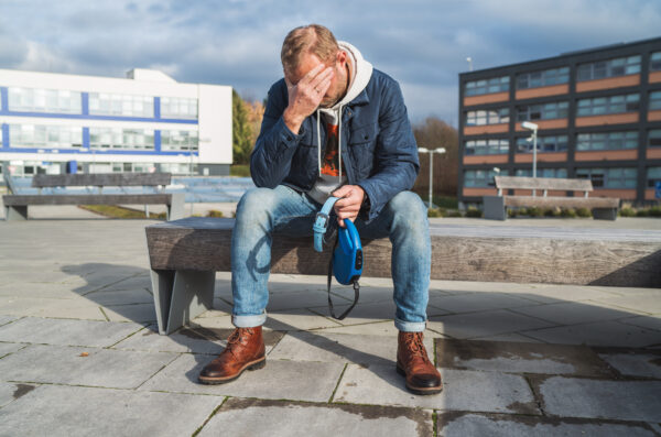 Broken with grief man dog owner is grieving sitting on a bench with the lovely pet collar and deep weeping about animal loss.